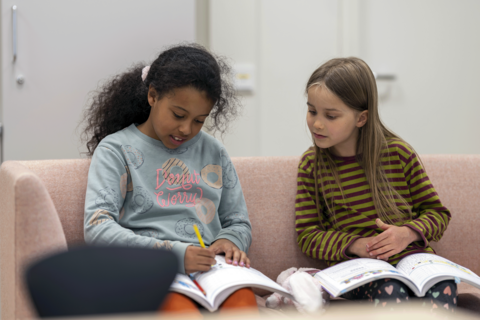 Kaksi lasta istuu sohvalla tehtäväkirjat sylissä ja tekee tehtäviä.