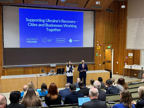 Kaksi ihmistä esiintymislavalla. Yleisössä ihmisiä.