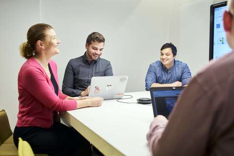 Three men and a woman at a table with laptops.