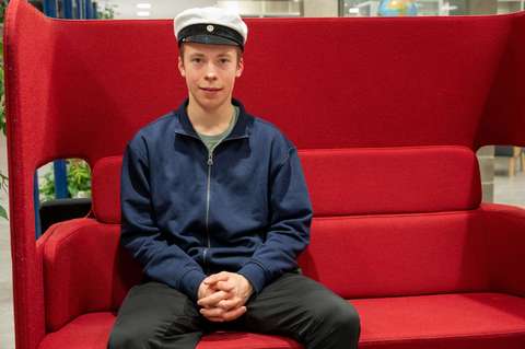 Henkilö istuu punaisella sohvalla ylioppilaslakki päässä