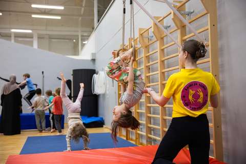 In the picture, a child is hanging upside down in a hoop. An adult is standing nearby and helping.