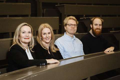 Neljä ihmistä istuu vierekkäin auditoriossa.