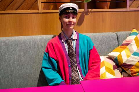 Henkilö istuu hymyilevänä sohvalla ylioppilaslakki päässä.