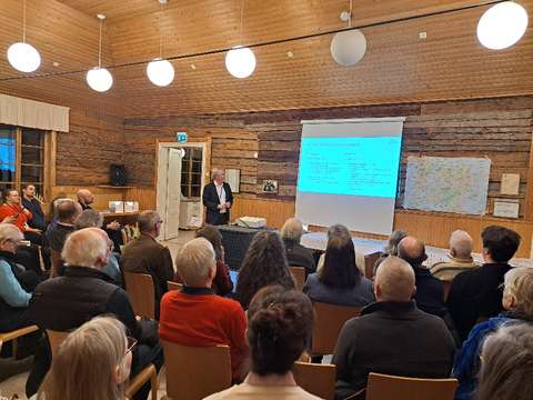 Valokuvassa henkilö pitää esitystä ja yleisö kuuntelee.