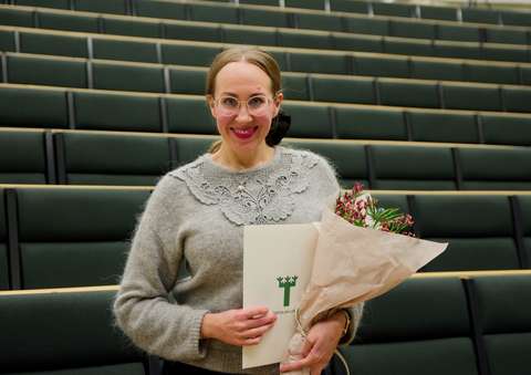 Nainen hymyilee kameralle diplomi ja kukkakimppu kädessään.