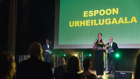 Kuvassa näkyy Espoon Urheilugaalan päälava. Lavalla seisoo kaksi Espoo Hall of Fame -kunniagallerian uutta urheilijaa jääkiekkoilija Timo Blomqvist ja purjehtija Tuuli Petäjä-Sirén.