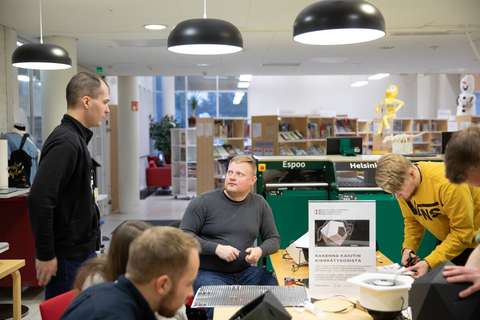 Henkilöitä keskustelee ja työskentelee yhteisen pöydän äärellä.