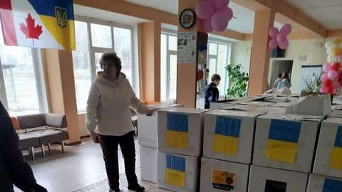 Nainen seisoo pahvilaatikoista koostuvan pinon vieressä. Laatikoissa näkyy ukrainan lipun värit.