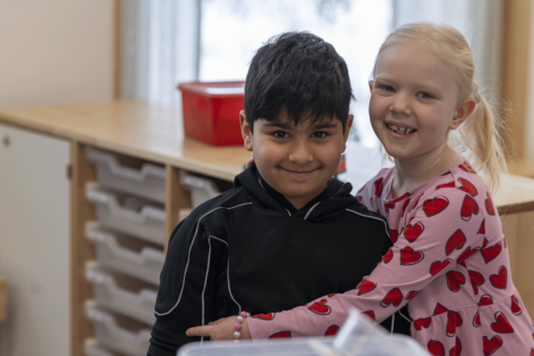 Kaksi lasta istuu vierekkäin ja hymyilee.