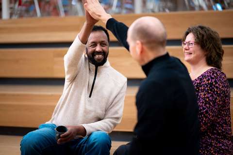 Iloisia ihmisiä toimistolla joista kaksi heittävät yläviitosen.