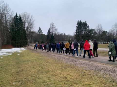 Nurmikkoisen maaston keskellä kulkevaa polkua kulkee suuri joukko ihmisiä. Taustalla puita ja siniharmaa taivas. 