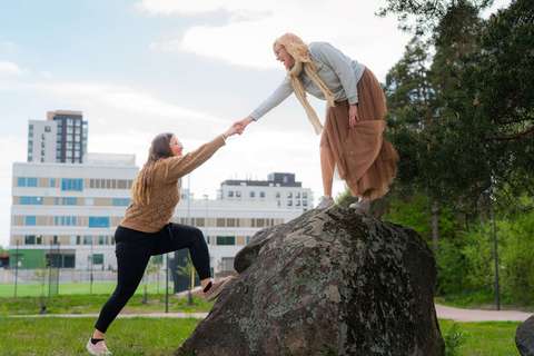 A person is standing on a large rock and is helping another person to climb it.