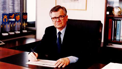 Espoon entinen kaupunginjohtaja Pekka Löyttyniemi istuu työpöydän ääressä puku päällä.