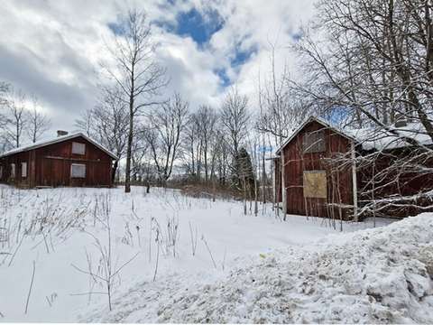Kaksi vanhaa punaista puurakennusta ja puita lumisessa maisemassa.