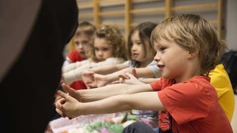Kuvassa lapset istuvat maassa vierekkäin ja venyttelevät käsiään.