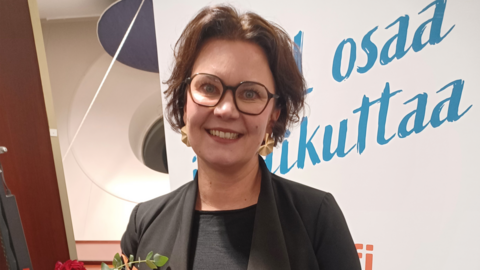 Silmälasipäinen henkilö hymyilee leveästi