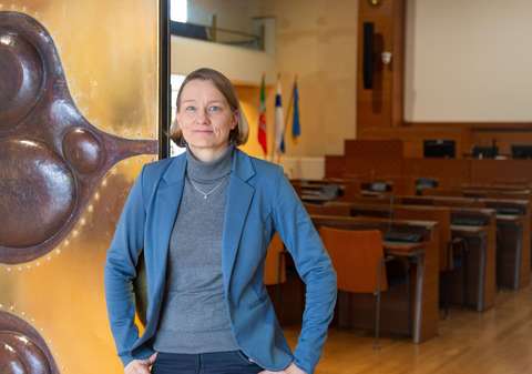 Henkilö seisoo avoinna olevan oven edessä ja takana näkyy pöytiä ja tuoleja salissa.