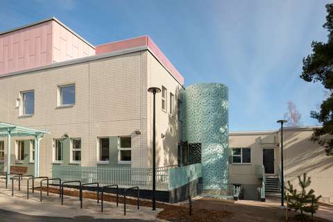 Espoonlahden terveysaseman julkisivu, jossa beigeä, turkoosia ja vaaleanpunaista, etualalla pyörätelineitä.