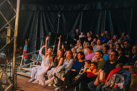 Kuvassa on sirkusteltassa istuvaa yleisöä, jotka hurraavat kädet ilmassa.