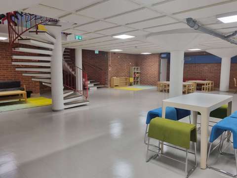 Punatiiliseinäinen erilaisin pöydin ja penkein sisustettu tilava kellarikerroksen tila.