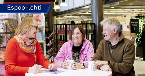Elina Pulli, Riitta Lukkaroinen-Mikkonen, and Pentti Mikkonen are sitting at a table and looking at each other.