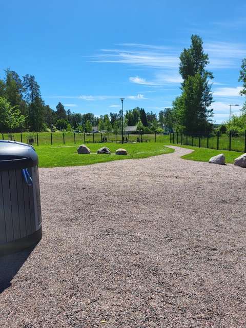 Hiekka-alue, joka on rajattu aidoin. Myös nurmikkoa, isoja kiviä ja roskapönttö.