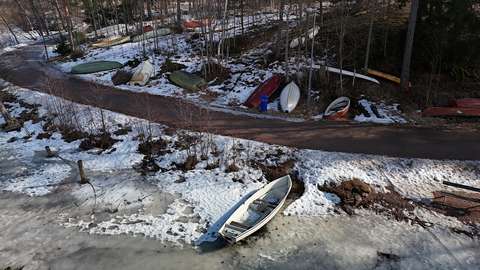 Luminen Pitkäjärven ranta, jossa useita veneitä rivissä maalla ja yksi jäällä, ilmakuva.