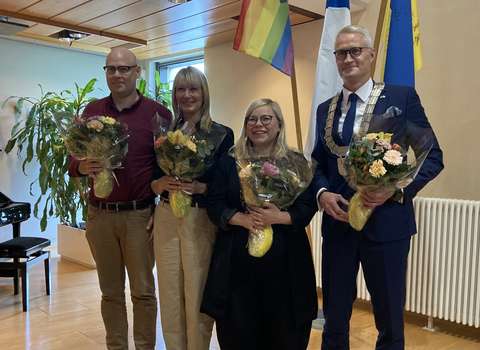 Espoon valtuuston puheenjohtajiston neljä henkilöä seisovat hymyillen rivissä ja kukkakimput käsissään.