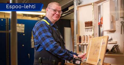Kimmo Fonsell is fastening the lid of a school desk with a screw and looking at the camera.