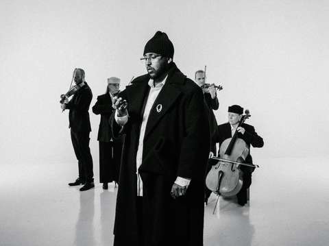 Tapiola Sinfonietta jousikvartetti soittaa taustalla ja etualalla Hassan Maikal katsoo kämmentään mustavalkoisessa kuvassa.