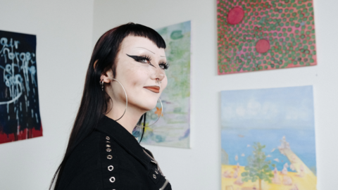 Goottityylisesti pukeutunut nuori hymyilee taidegalleriassa.