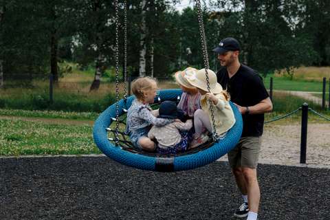Aikuinen keinuttaa lapsia asukaspuiston keinussa