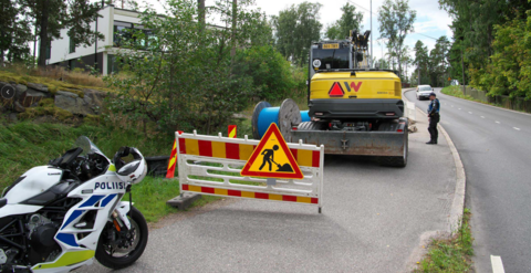 Poliisimoottoripyörä ja kaivinkone katutyömaalla.