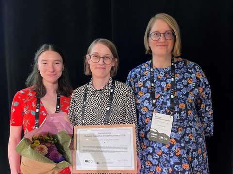 Kolme henkilöä hymyilevät, he ovat saaneet palkinnoksi diplomin.
