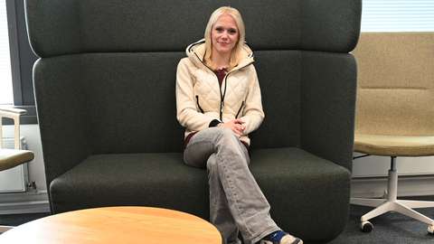 A smiling blonde student is sitting on a green sofa.