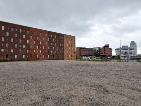 Etualalla hiekkakenttä, taustalla punatiilisiä ja vaalea rakennus.