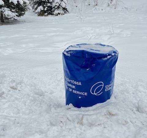 Sininen huputettu roska-astia lumessa.