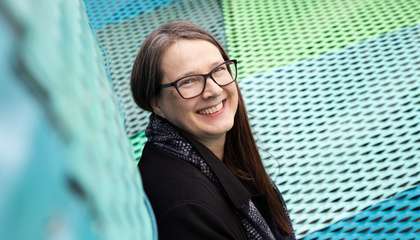 hymyilevä nainen katsoo turkoosinväristen metallipintojen välistä.