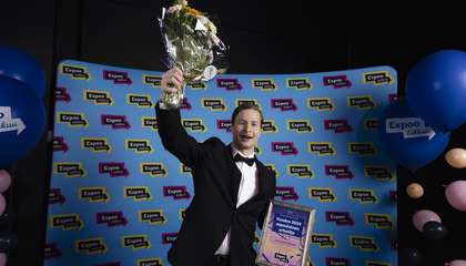 Kuvassa nuori mies tuulettaa kukkakimppu ja palkintotaulu kädessään.