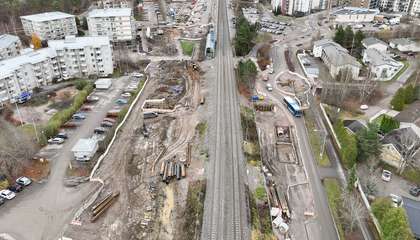 An aerial photo of the Kilo railway station area. There are railway tracks in the centre and a construction site around the tracks. There are parking lots, streets and residential buildings around the construction site.