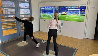 Kaksi oppilasta pelaamassa liikuntapeliseinällä jalkapalloa.