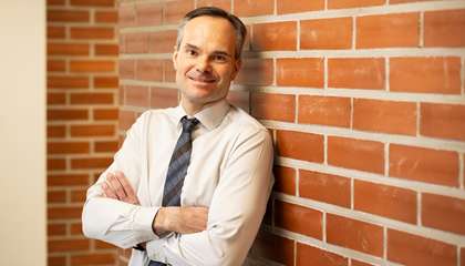 Kaupunginjohtaja Kai Mykkänen nojaa tiiliseinään ja hymyilee, puolivartalokuva.