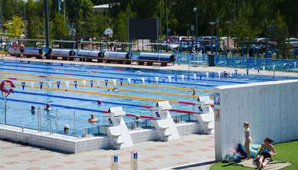 The picture shows the outdoor swimming pool in Leppävaara on a summer day. There are people in the pool and around it.