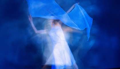 Epätarkka kuva liikkuvasta tanssijasta, jolla heiluttaa käsissään kangasta.