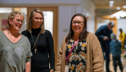 Tre anställda inom småbarnspedagogik står i daghemmets korridor och ler.