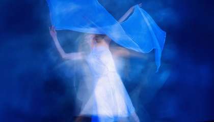 Valkoiseen pukeutunut henkilö tanssii huivin kanssa.