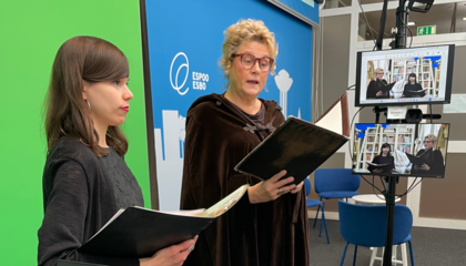 Inari Mykkänen ja Pirkko Ilmanen seisovat studiossa greenscreenin edessä. Sivulla olevalla näytöllä näkyvät esiintyjät taustallaan kirjahylly.