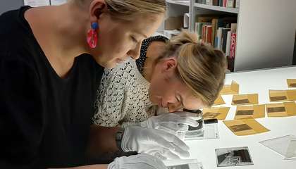 Two people bent over a glass table looking at photographic negatives.