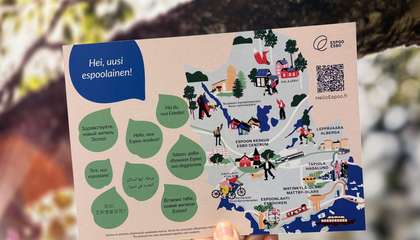 Käsi pitelemässä postikorttia, jossa on tervehdyksiä eri kielillä ja karttakuva Espoosta.