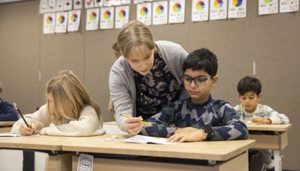 Opettaja neuvoo oppilasta, joka istuu pulpetissa ja tekee tehtäviä.